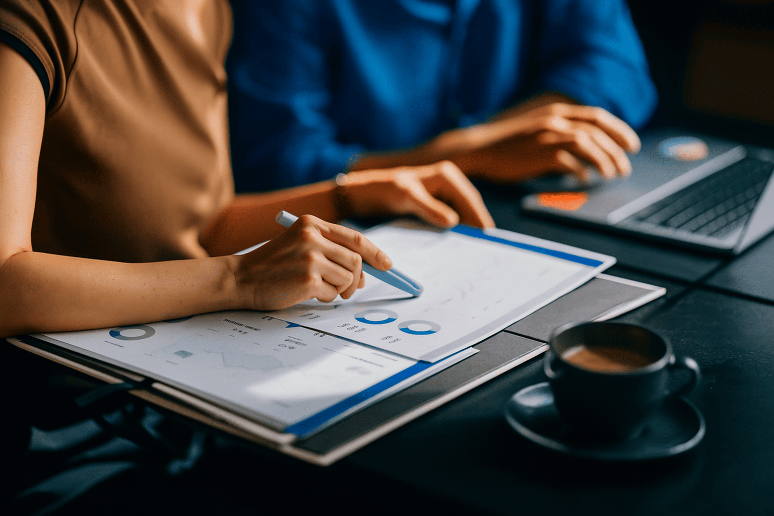 Two people analyse financial data and investment strategies using documents and a laptop.